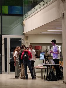 Zespół trzyosobowy stojący przed punktem rejestracyjnym, z grupą stoi jeden z organizatorów, za biurkiem z komputerami stoi drugi organizator. 